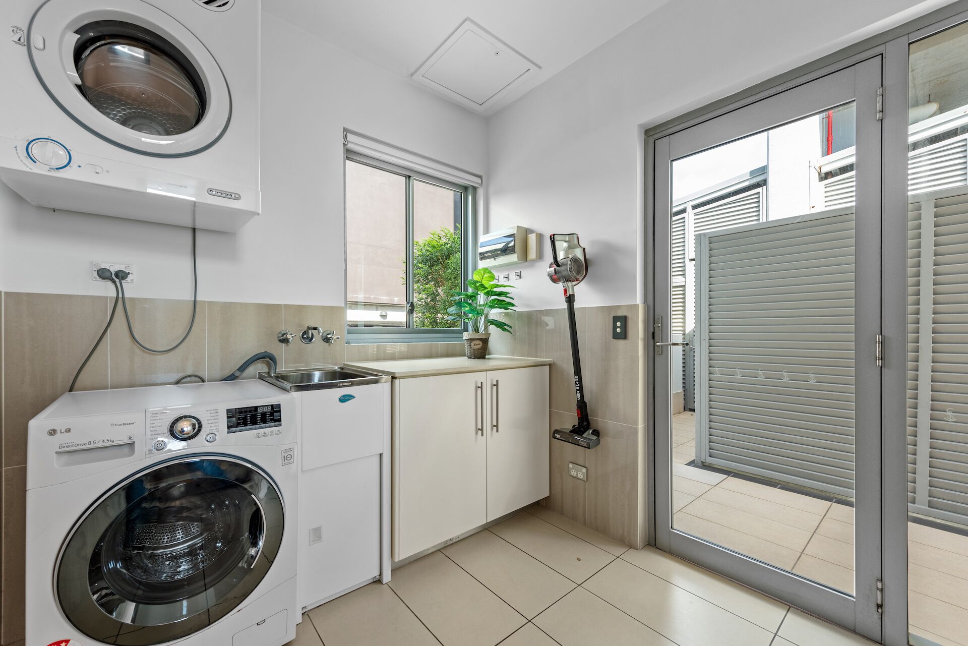 A compact laundry room with a front-loading washing machine, a sink, and a window.