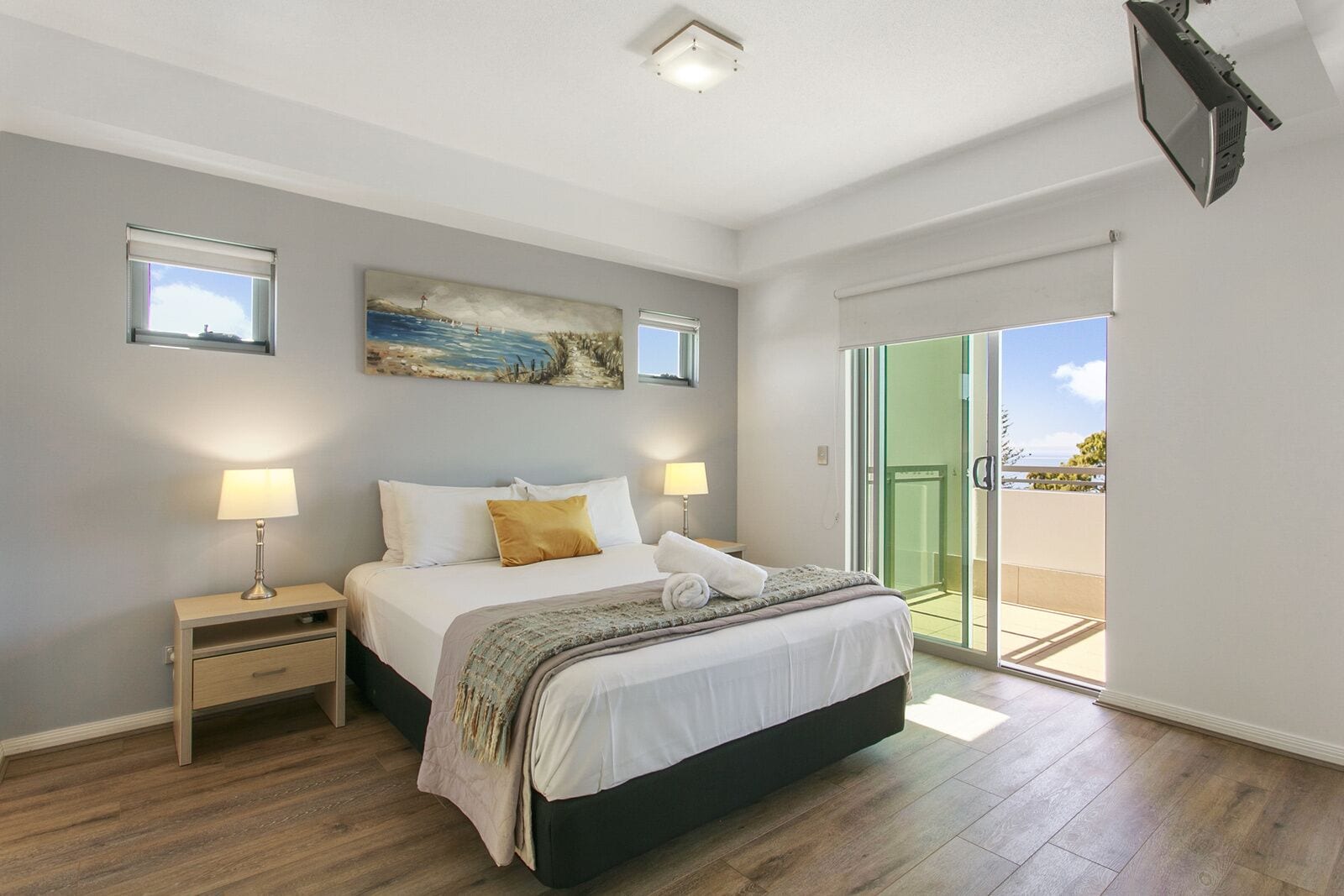 Un dormitorio moderno con una cama grande, lámparas de noche, un cuadro y una puerta corrediza de vidrio a un balcón.