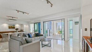 A spacious living room with a sofa, chairs, a coffee table, and a dining area. - Proximity Waterfront Apartments (Redcliffe)