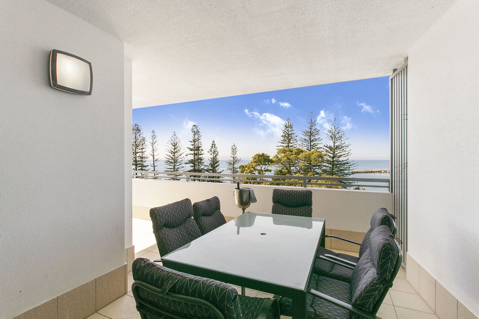 A balcony with a table and chairs, a view of trees and a body of water.