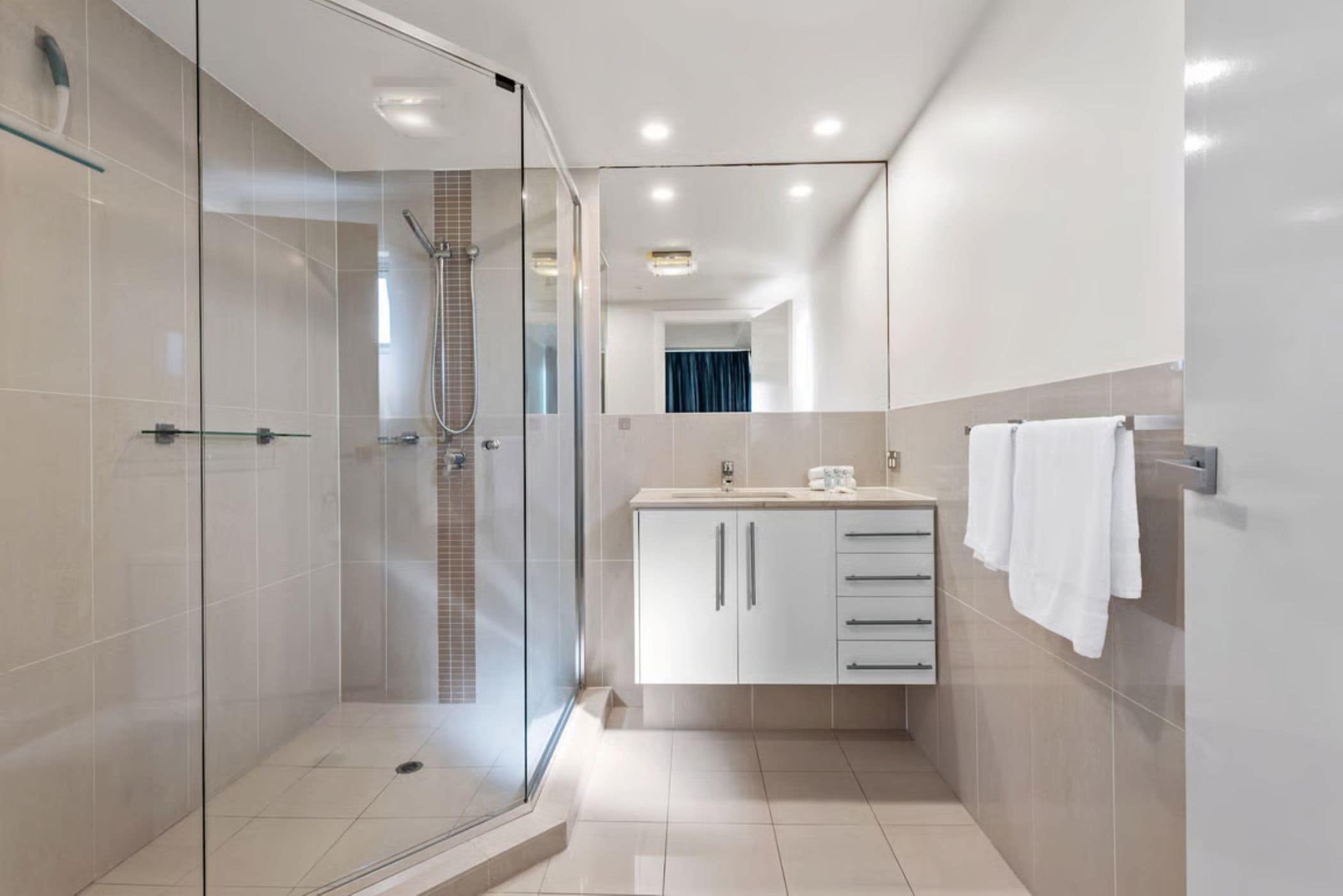 A modern bathroom with a glass-enclosed shower, a white vanity with drawers, and a mirror above the sink.