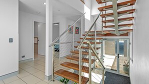 A modern staircase with wooden steps and metal railings, leading to a second-floor area with a view of the outdoors. - Proximity Waterfront Apartments (Redcliffe)