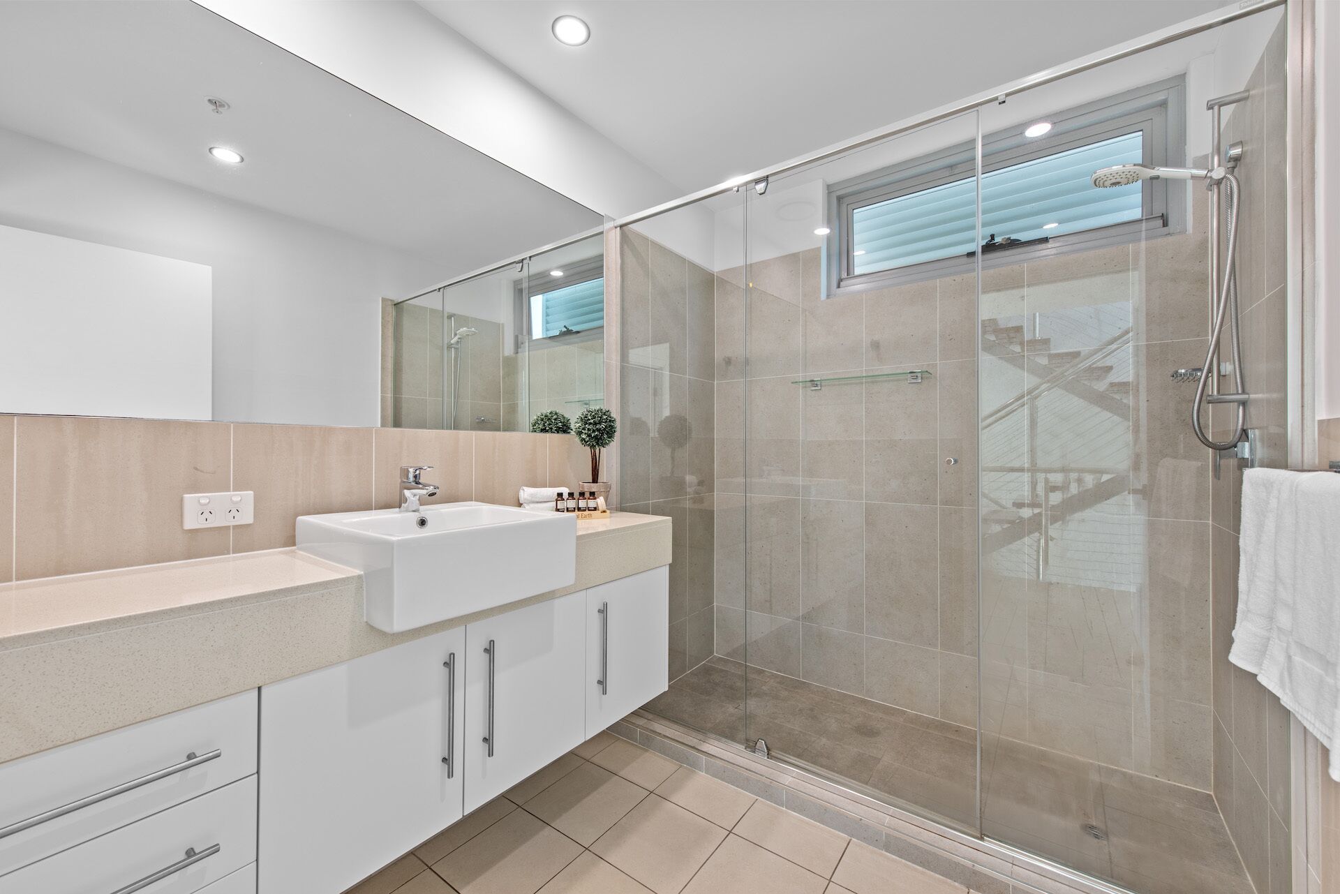 A modern bathroom with a glass-enclosed shower, a white sink, and a large mirror.