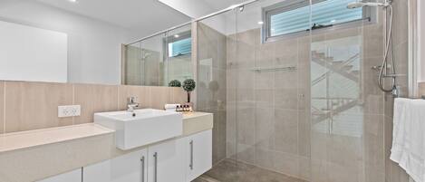 A modern bathroom with a glass-enclosed shower, a white sink, and a large mirror.