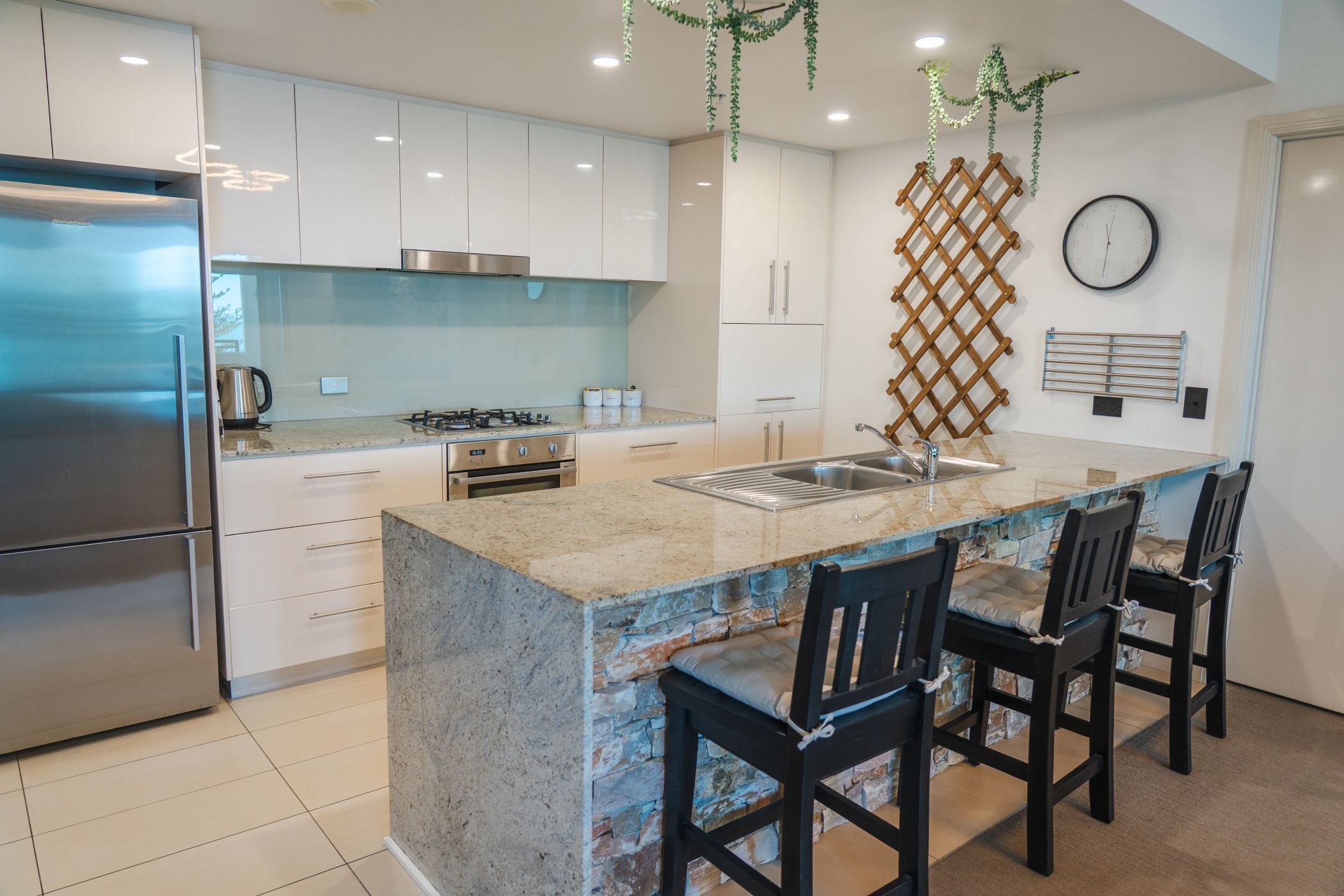 A modern kitchen with a central island, stainless steel appliances, and a hanging plant decoration.