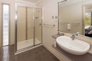 Une salle de bain moderne avec une douche à l’italienne en verre, un lavabo blanc et un grand miroir.