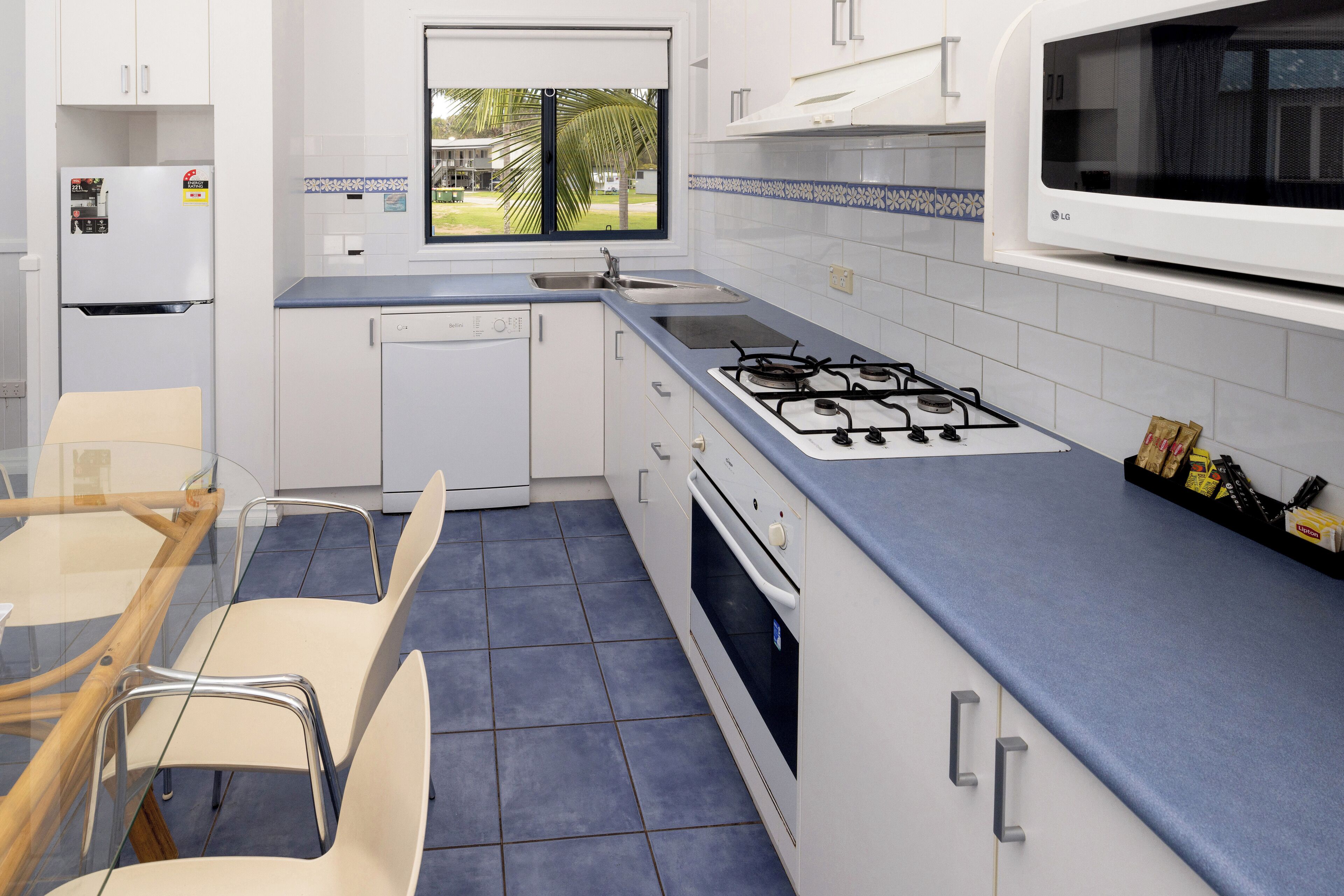 Une cuisine moderne avec des armoires blanches, une cuisinière à gaz, un lave-vaisselle et une fenêtre donnant sur l’extérieur.