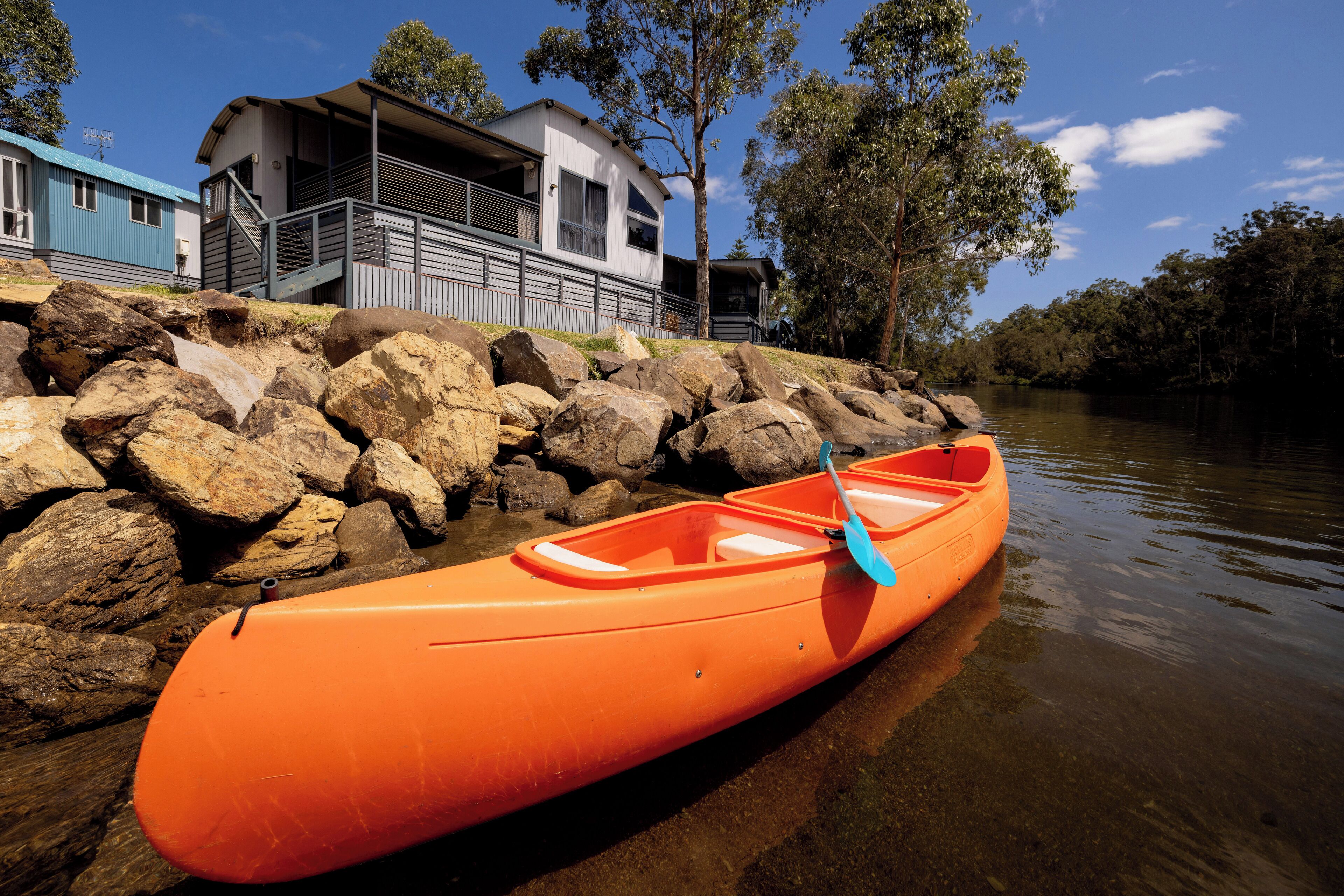 A canoe tied to a rocky shore with a house in the background.