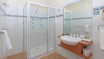 Ein Badezimmer mit einer gläsernen Duschkabine, einem Waschbecken mit Spiegel darüber und weiß gefliesten Wänden.