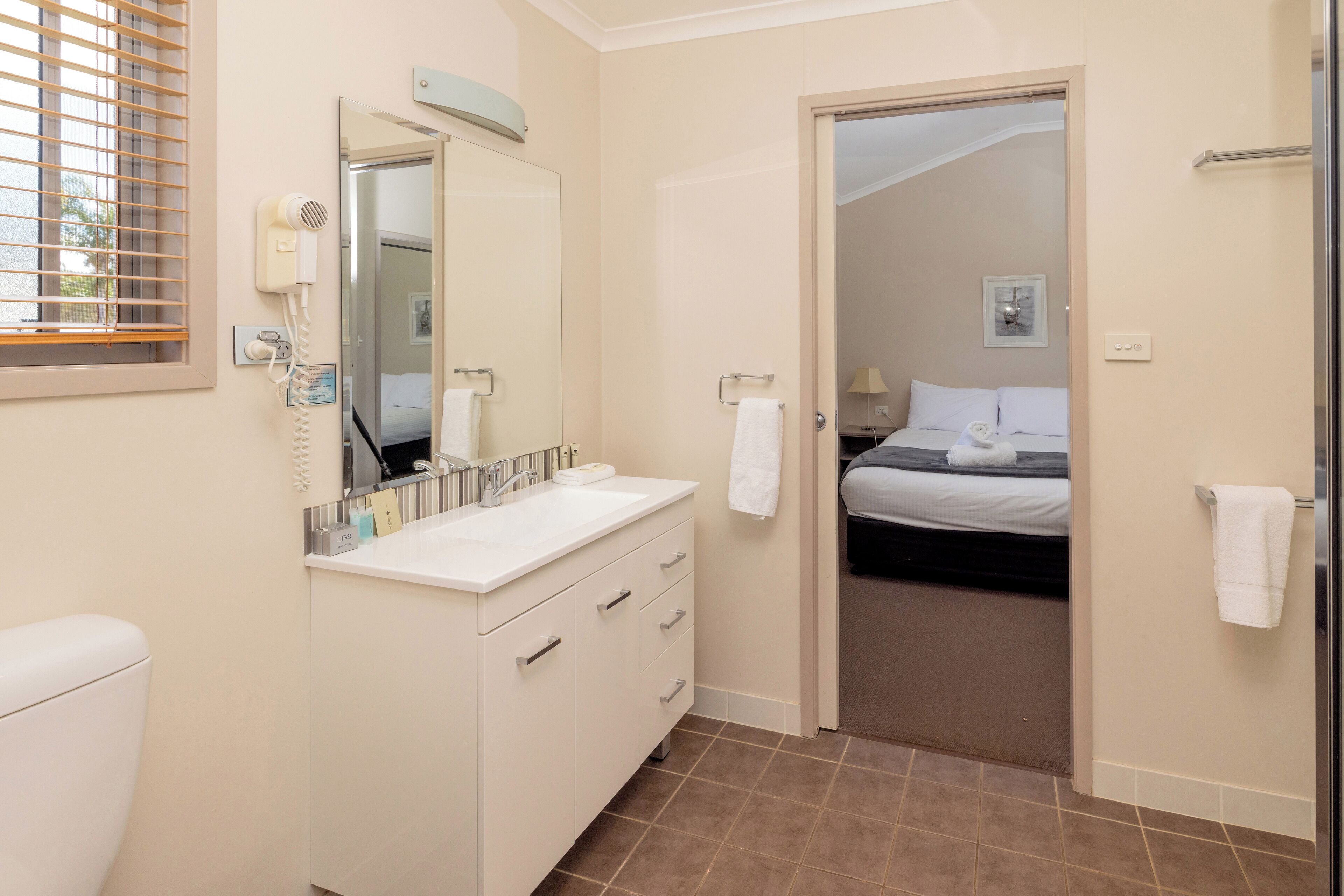 A modern bathroom with a white sink, mirror, and toilet. There is a hairdryer on the wall and a towel rack.