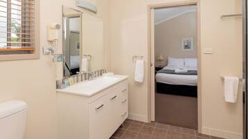 A modern bathroom with a white sink, mirror, and toilet. There is a hairdryer on the wall and a towel rack.