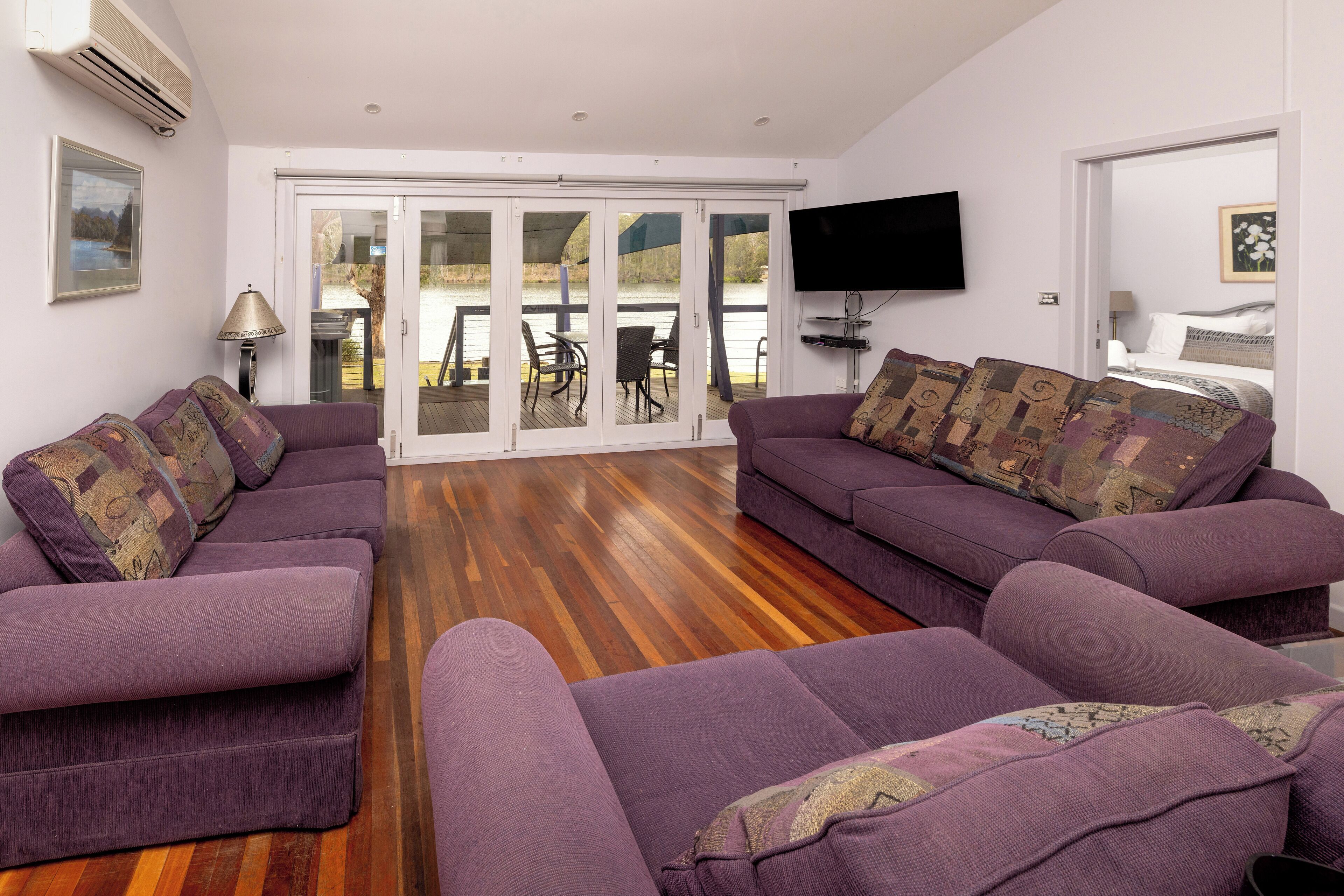 Ein Wohnzimmer mit zwei violetten Sofas, einem Flachbildfernseher und einer Schiebetür zu einem Außenbereich.
