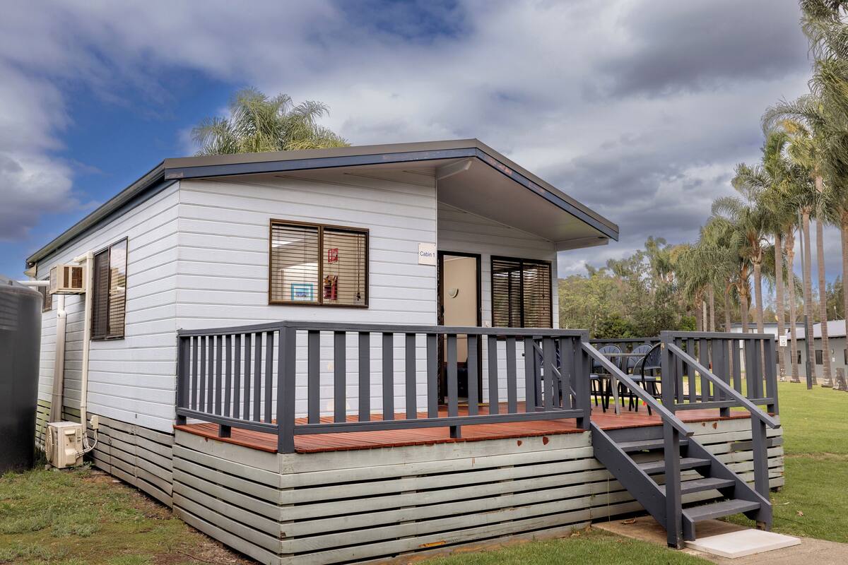 A single-story cabin with a wooden deck and a staircase leading to the entrance.