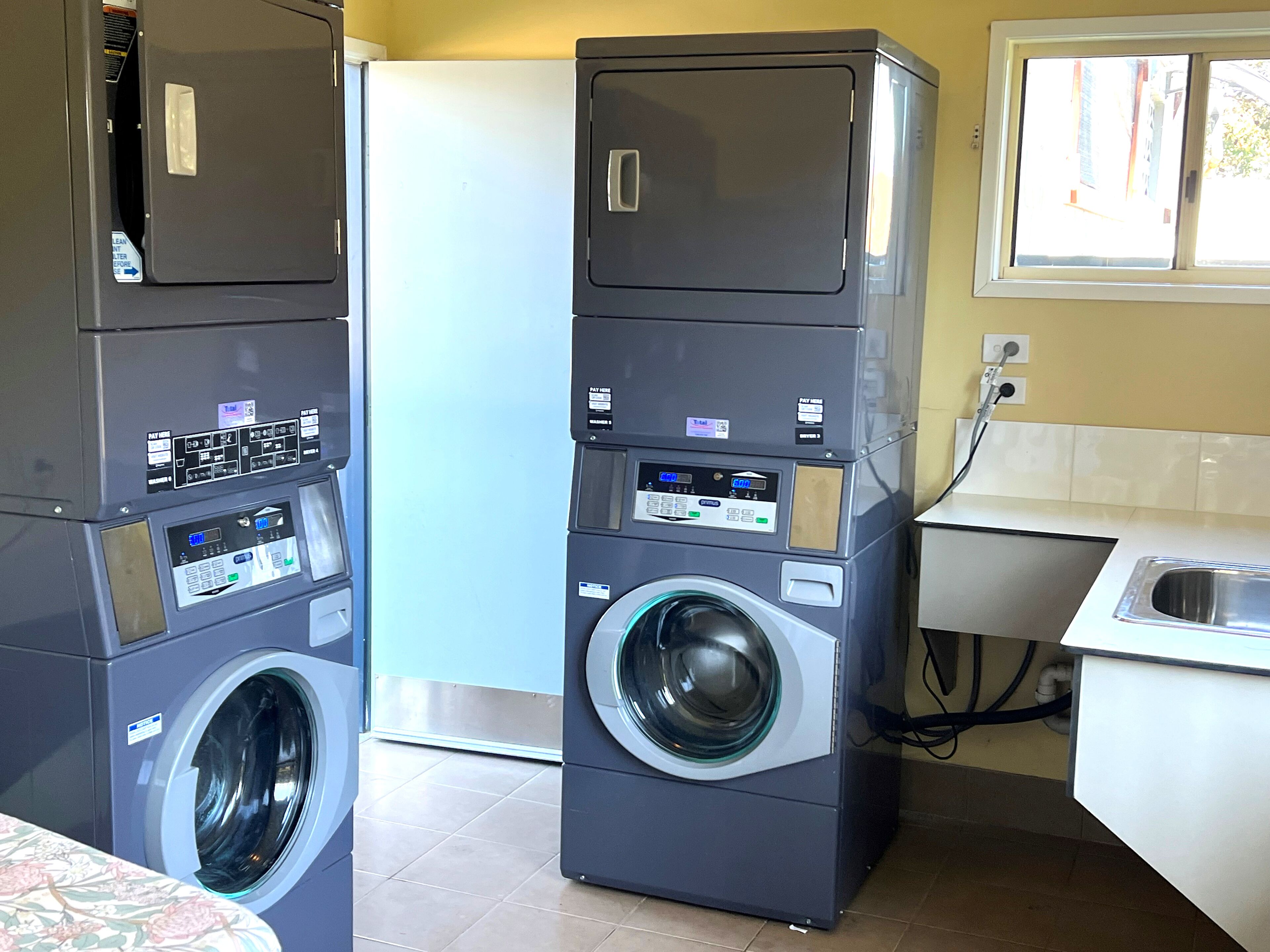 A laundry area with stacked washing machines and a dryer, a sink, and a window with blinds.