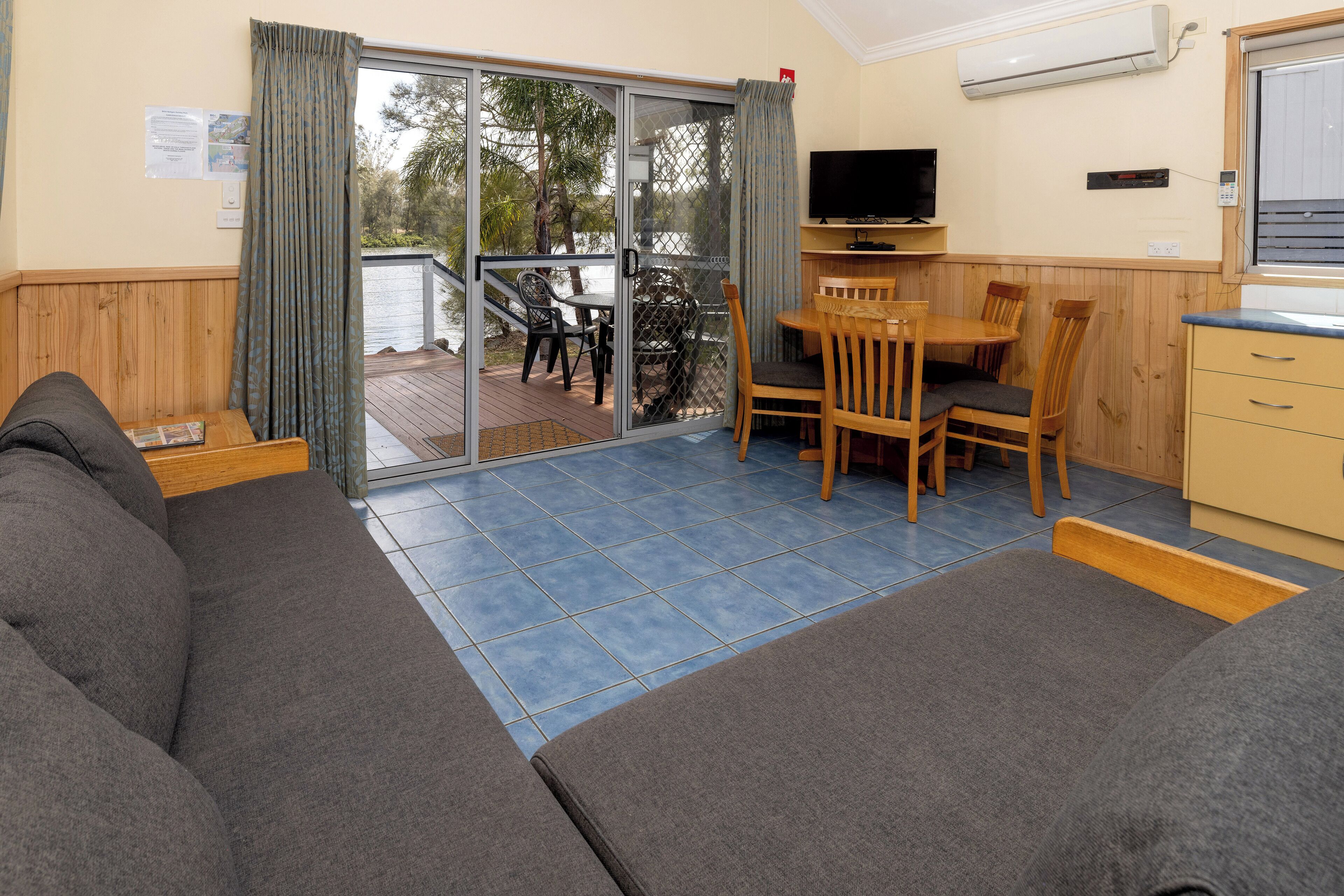 Una habitación con sofá, una mesa de comedor con sillas, televisión y puerta corrediza de vidrio que da a una terraza exterior.