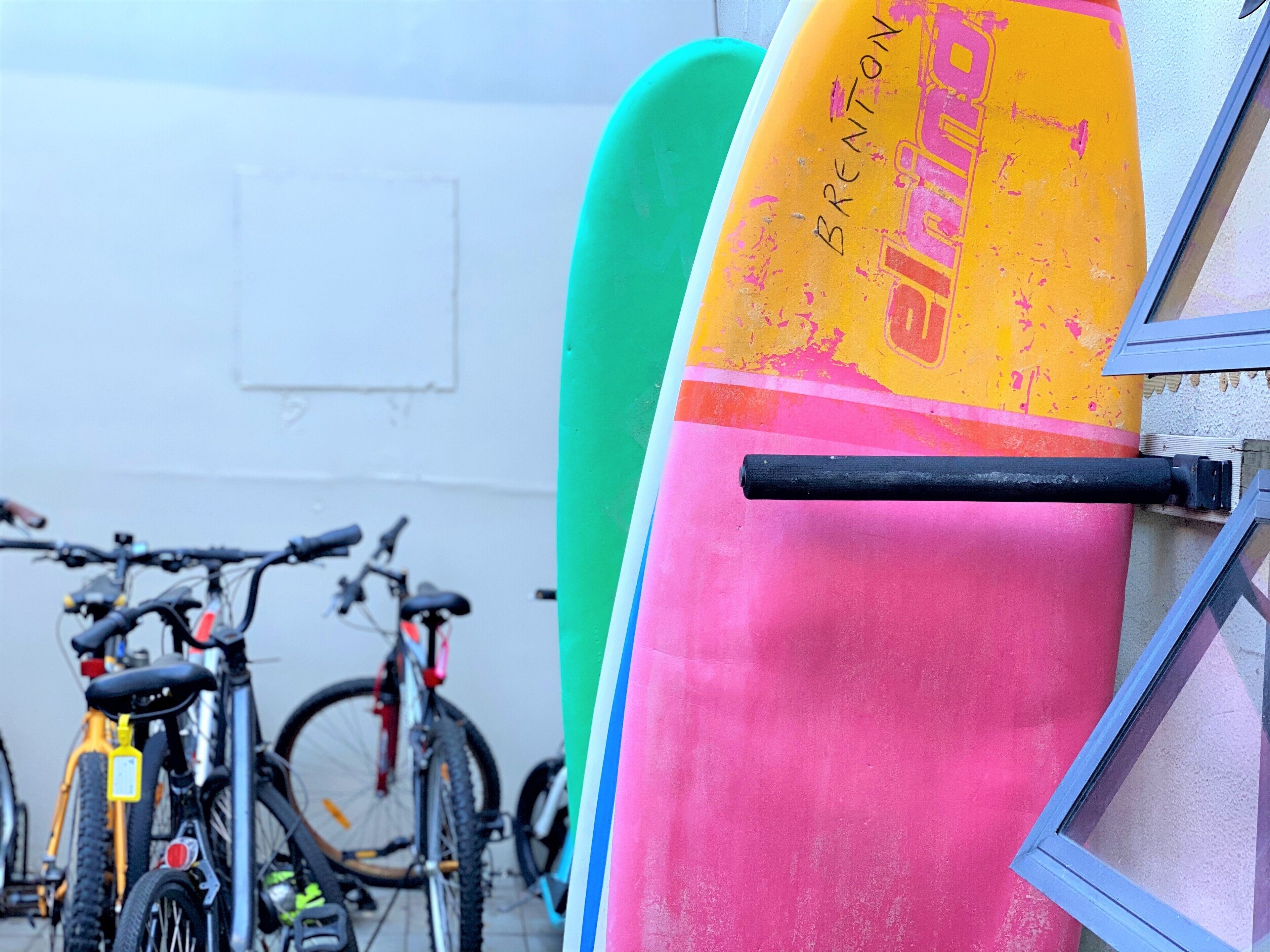 A surfboard leaning against a wall with a bicycle in the background.