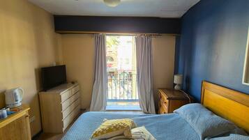 A hotel room with a bed, a television, a desk, and a window with curtains.