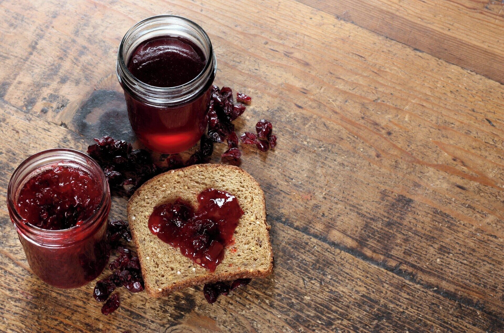 A slice of bread with jam and a jar of jam on a wooden surface.