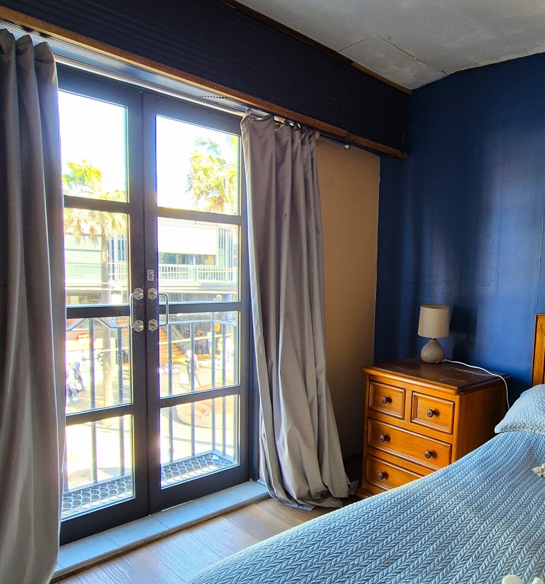 A room with a sliding glass door, a wooden dresser, and a bed with a blue patterned bedspread.