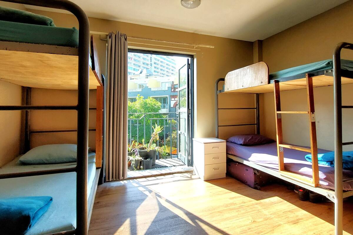 A dormitory room with bunk beds, a small table, and a window with curtains.