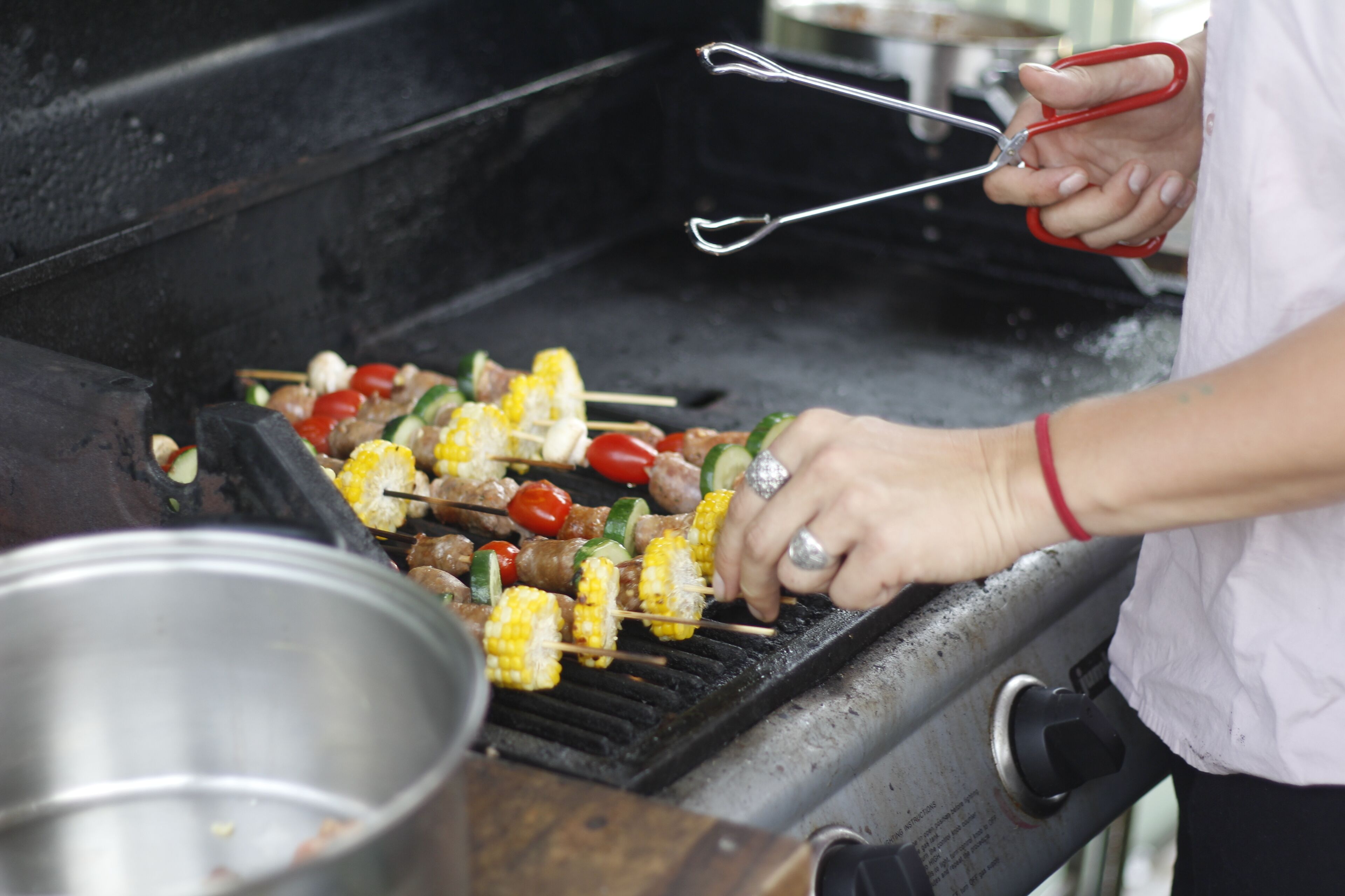 Una persona asando brochetas de carne y verduras en una parrilla al aire libre.