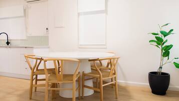 A round dining table with four wooden chairs, a potted plant, and a window with a white blind.