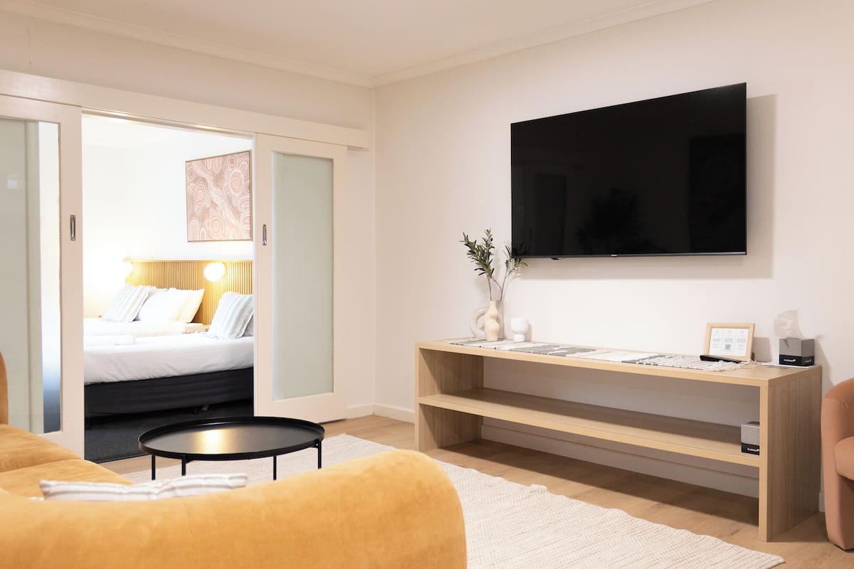 A modern hotel room with a bed, a sofa, a desk, and a TV.