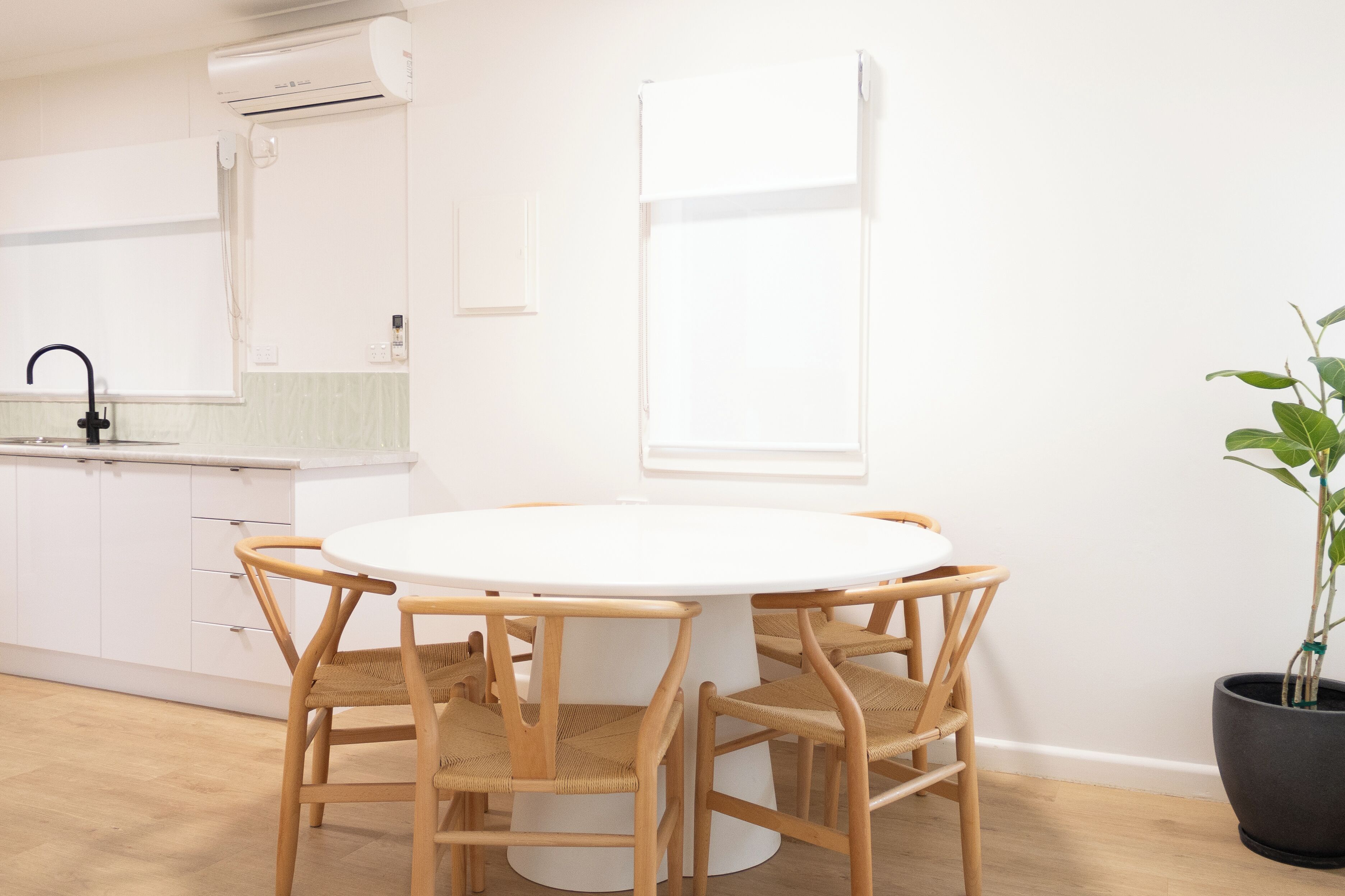 A modern kitchen with white cabinets, a round white table, and four wooden chairs.