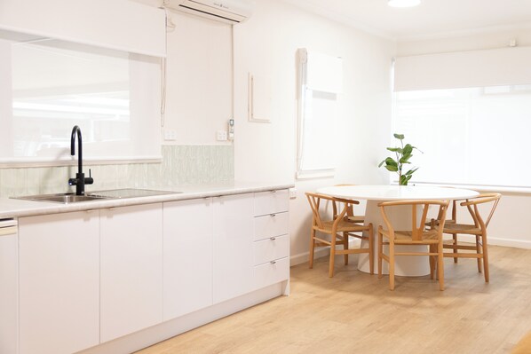Une cuisine moderne avec des meubles blancs, un robinet noir et une table ronde en bois, accompagnée de chaises.