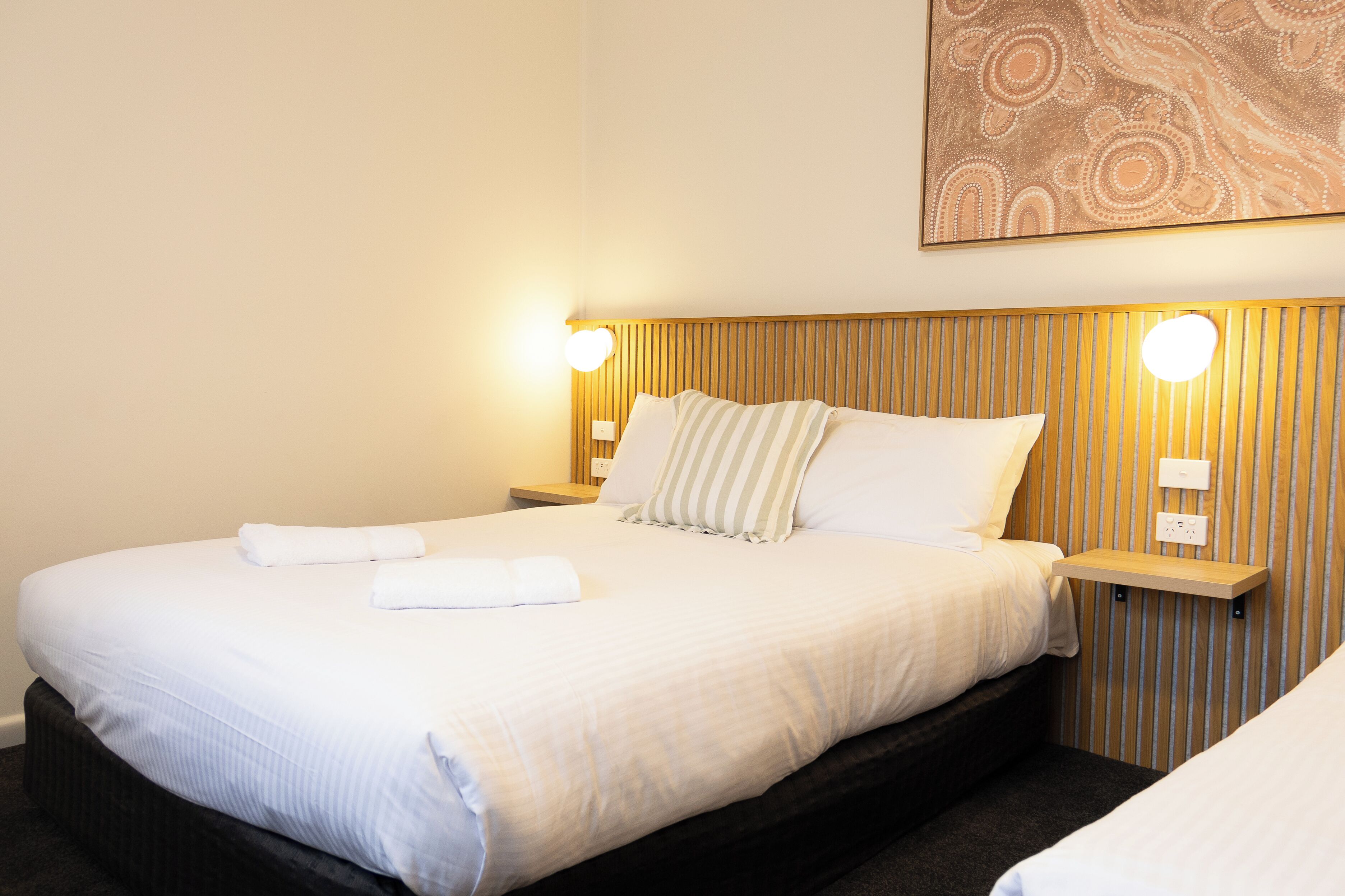 A neatly made bed with white linens, two bedside lamps, and a wall-mounted light fixture.