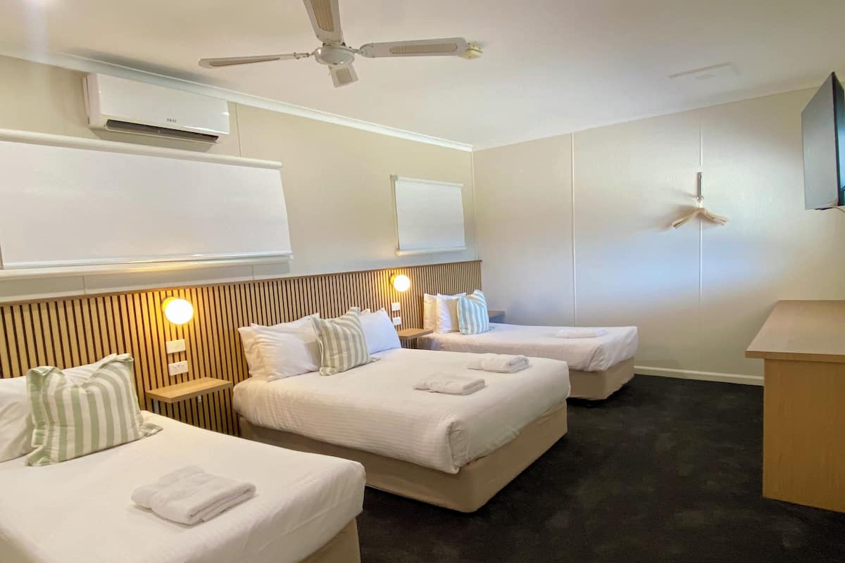 A hotel room with two beds, a ceiling fan, a mounted TV, and a bedside table with a lamp.