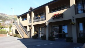 A two-story building with a staircase leading to the upper floor, large windows, and flower boxes on the balconies. - Tresori Motor Lodge (Akaroa)