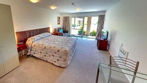 A bedroom with a large bed, a desk, a chair, and a TV. - Tresori Motor Lodge (Akaroa)