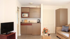 A compact living space with a kitchenette, a television, a sofa, and a small table with flowers. - Tresori Motor Lodge (Akaroa)