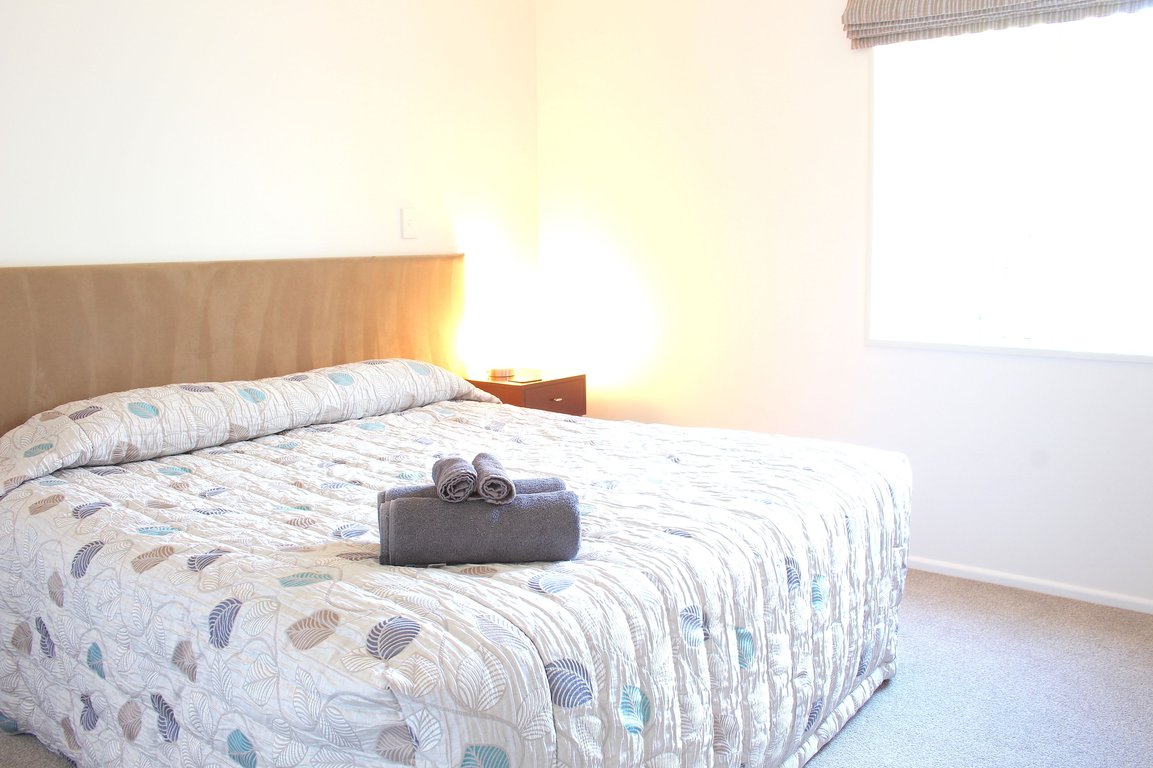 Una cama bien hecha con una colcha estampada y una toalla enrollada encima.