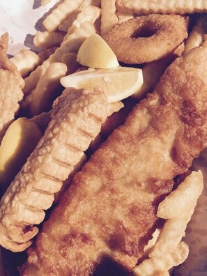 Primer plano de una variedad de mariscos fritos, incluyendo filetes de pescado rebozado y aros, con gajos de limón.