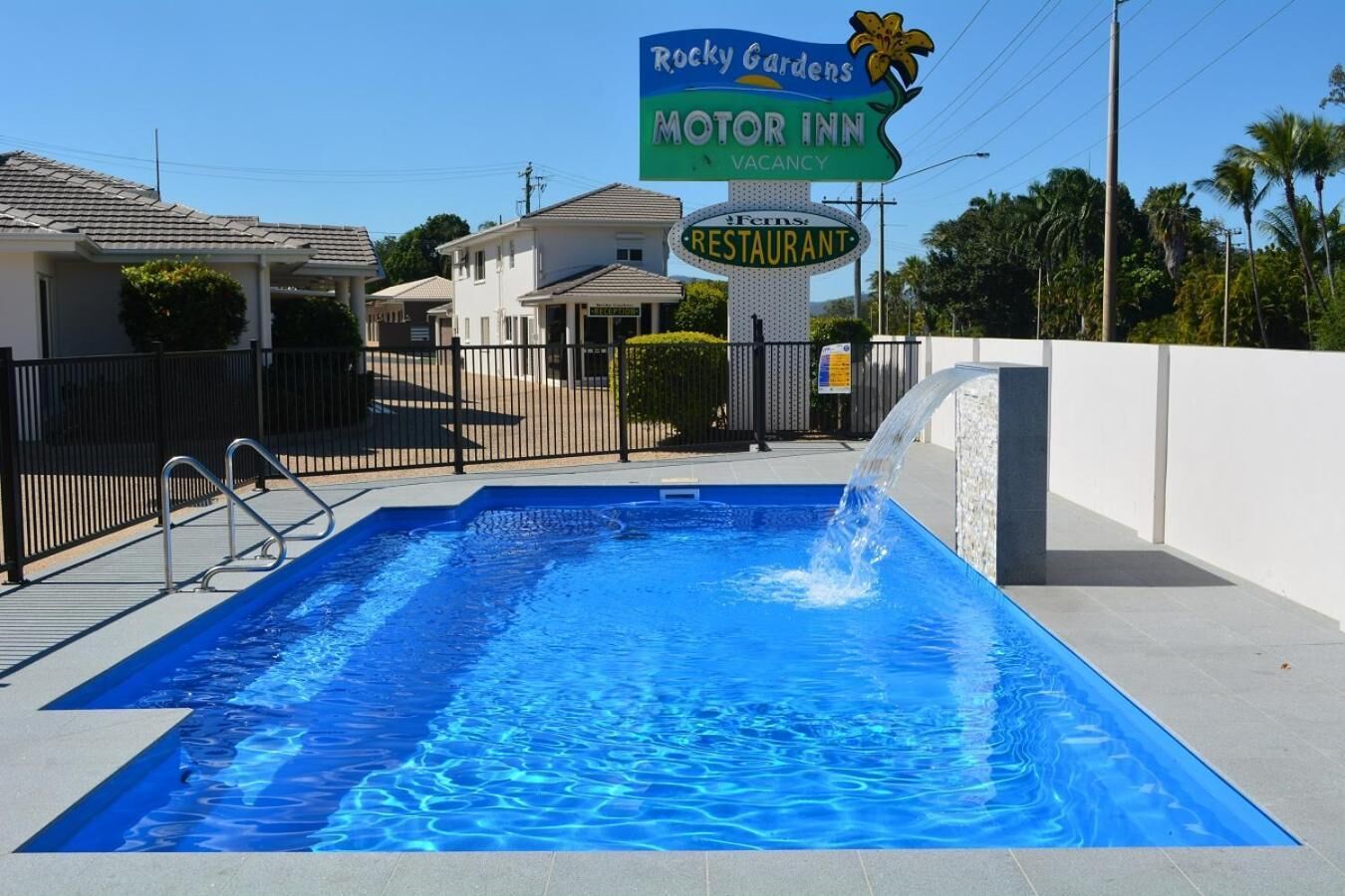 En swimmingpool med et skilt for Rocky Gardens Motor Inn og Ferns Restaurant.