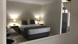 Un dormitorio con cama, mesitas de noche, lámparas, un escritorio y un espejo.