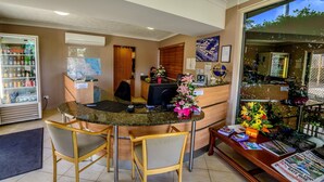 Un área de recepción con mostrador, dos sillas, un refrigerador con bebidas, un mapa y un arreglo floral.