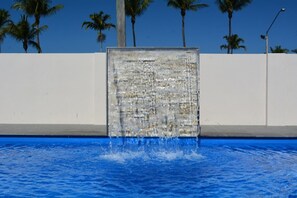 A pool with a waterfall feature and palm trees in the background. - Rocky Gardens Motor Inn (Allenstown)
