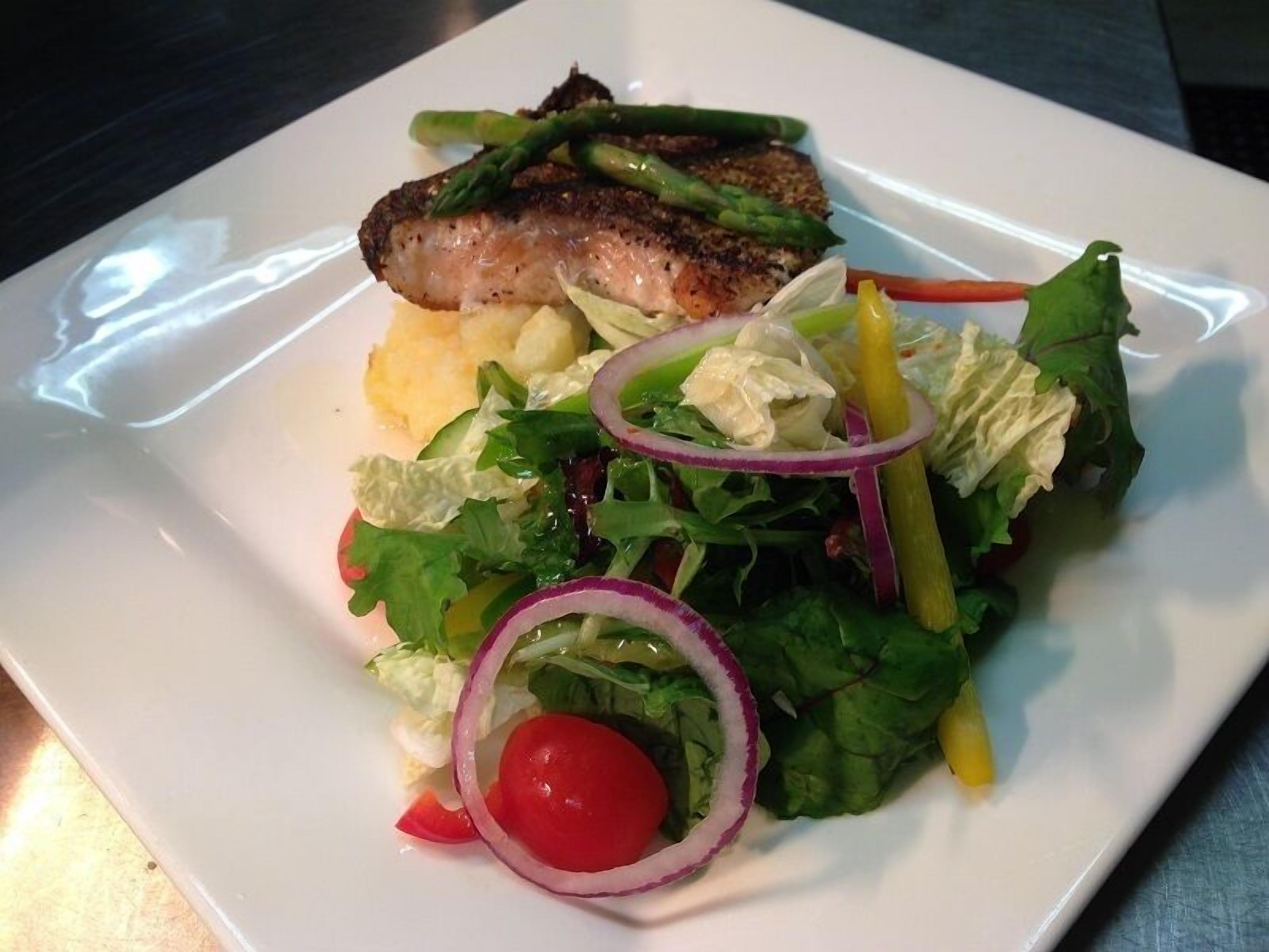 Un plato con pescado a la parrilla, guarnición de patatas y ensalada verde mixta.