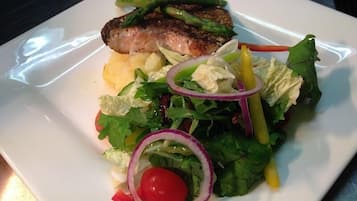 Un plato con pescado a la parrilla, guarnición de patatas y ensalada verde mixta.