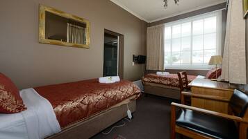 A hotel room with two beds, a desk, a chair, a TV, and a window with curtains.