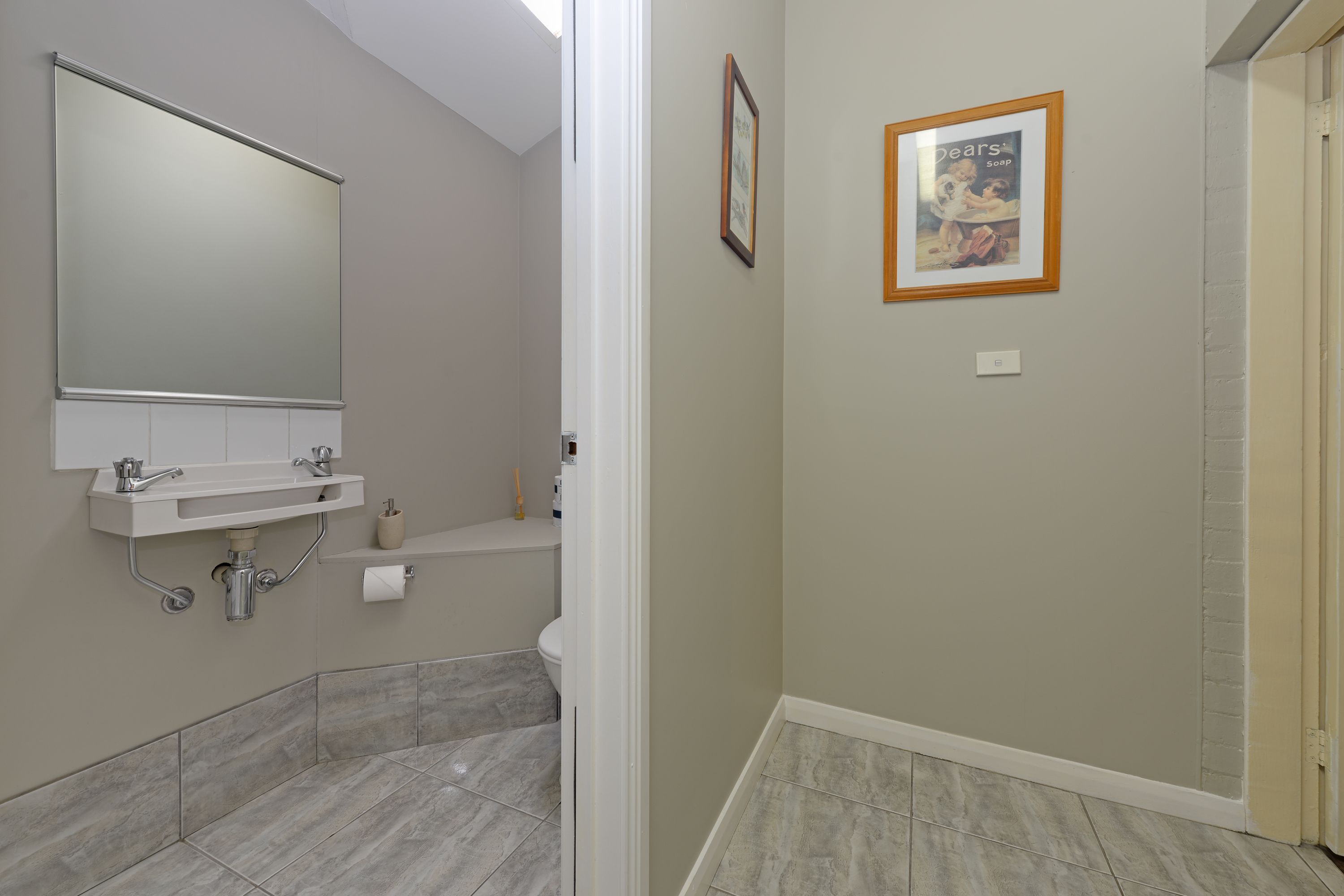 Ein Badezimmer mit großem Spiegel, Waschbecken und Toilette. An der Wand befinden sich zwei Bilder in Rahmen.