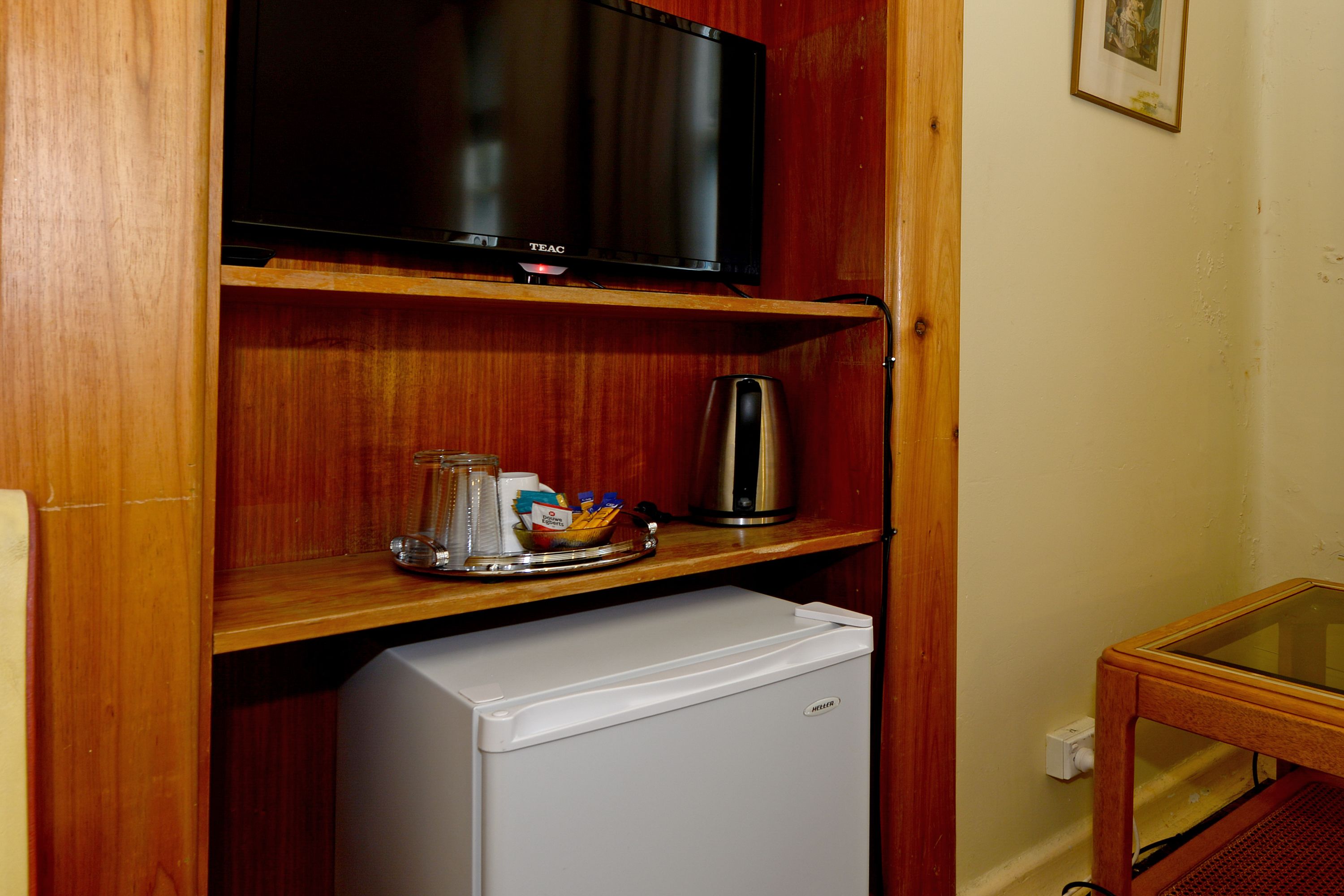 Una kitchenette compacta equipada con televisión, cafetera y refrigerador pequeño.