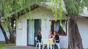 Een klein huis met een gevel van natuursteen, een veranda met witte stoelen en een tafel met een gele tafelkleed.