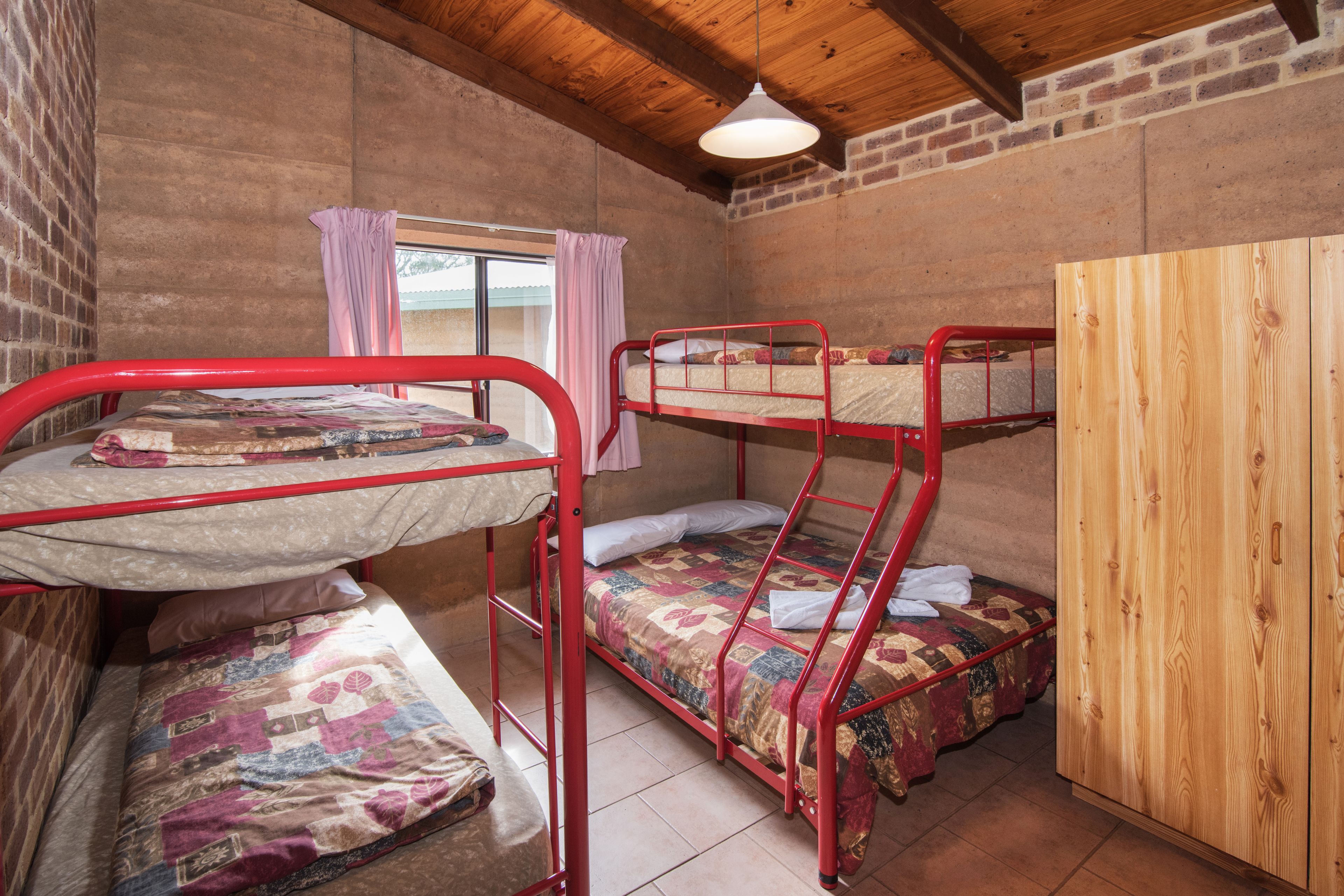 A bunk room with two bunk beds, a wooden wardrobe, and a window with curtains.