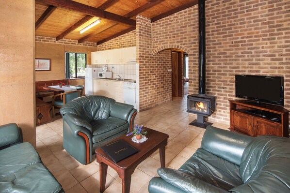 A cozy living room with leather sofas, a wooden coffee table, a fireplace, and a kitchen area in the background. - Sandy Bay Holiday Park (Broadwater)