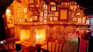 A bar area with a stone fireplace, wooden chairs, and a bar counter with various items and framed pictures. - Darcy Arms Motel (Surfers Paradise)