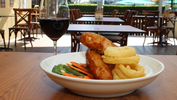A bowl of food with sausages and onion rings on a table, with a glass of red wine beside it. - Darcy Arms Motel (Surfers Paradise)